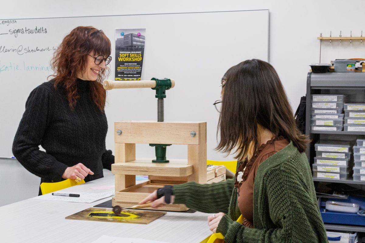 Liz Eckrote, a literature grad student, and Karsen Westhoff, a junior majoring in secondary English education use a presser to make valentines hearts. The tool presses Valentine's messages using ink into the paper.