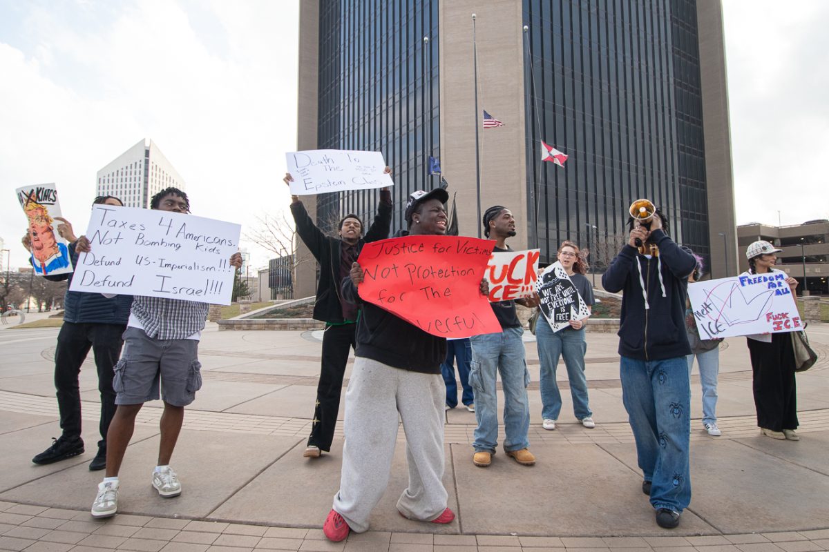 A group of protesters yell towards a passing car as the driver honks and waves in support.
