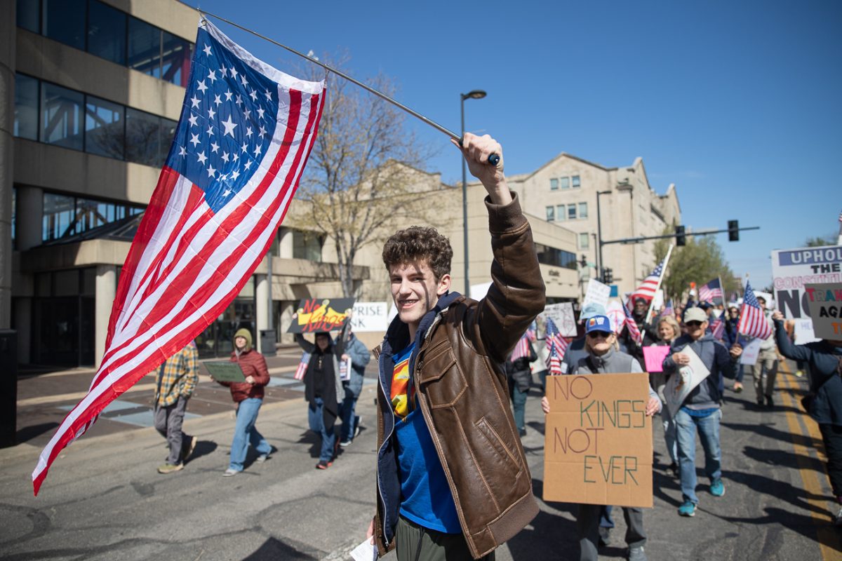 Jackson Rukes, 17, holds up a 35-star American flag from when Kansas was admitted into the union while attending the No Kings protest on Saturday, March 28, 2026. (KMUW)
