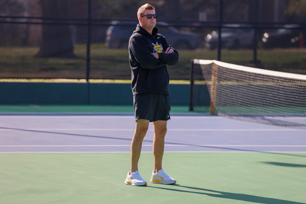 Wichita State women's tennis coach Jacob Eddins folds his arms during a match against South Florida March 27 at the Sheldon Coleman Tennis Complex. The Shockers won their 13th-consecutive game against the Bulls.