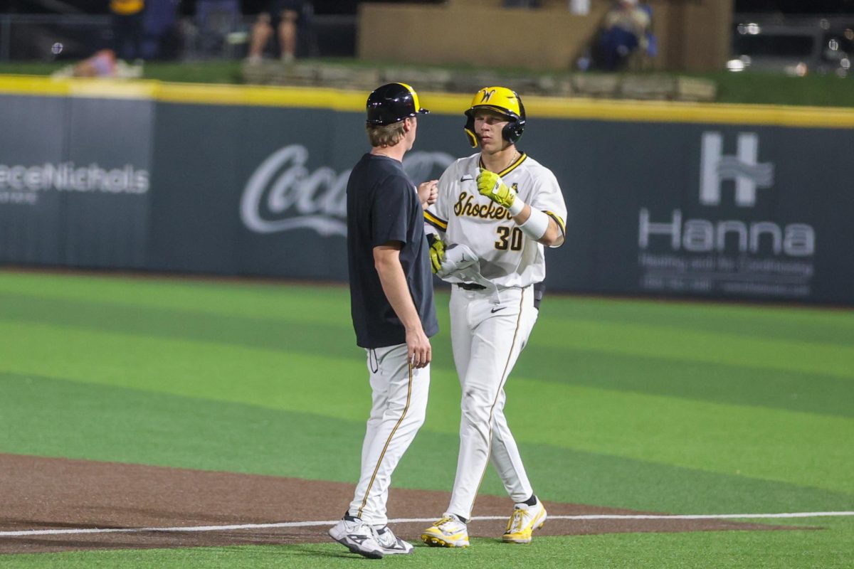 Wichita State baseball junior outfielder Anthony Cepeda (30) fist bumps graduate assistant Aaron Shellenberger at first base against Charlotte on March 20 at Eck Stadium. Cepeda reached first on an infield single.