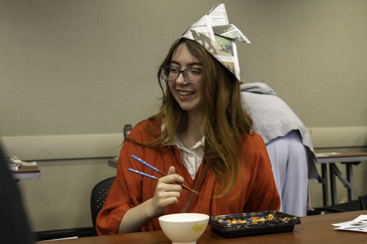 A participant of the Japanese Festival wears a hat made from origami while playing a chopstick game with m&ms.