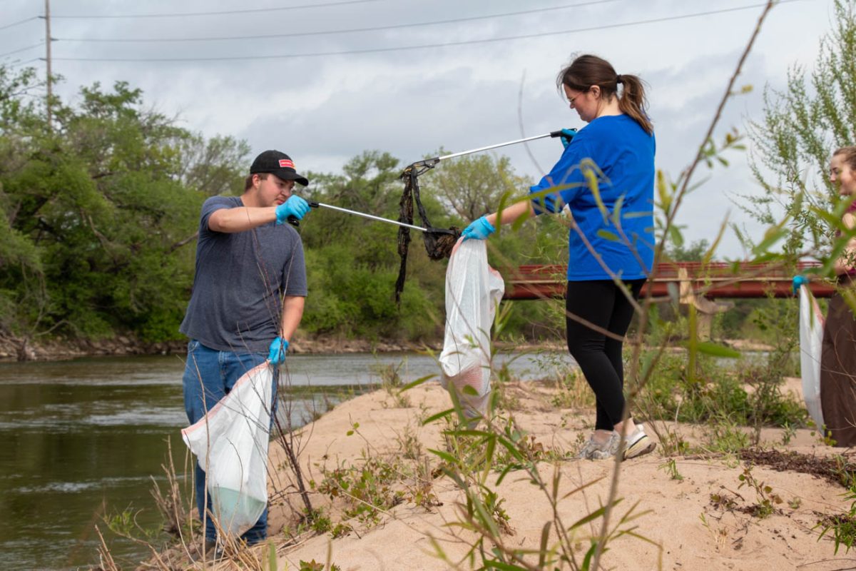 Justin Stanyer and Taryn Lessard team up to bag a particularly sprawling piece of trash at Wichita Clean Streams. Stanyer is an alum while Lessard is a current Wichita State student.