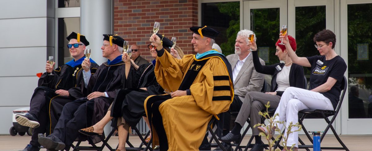 Wichita State deans raise champagne flutes in honor of 2026 graduates. Graduates were given commerative WSU-branded champagne flutes.